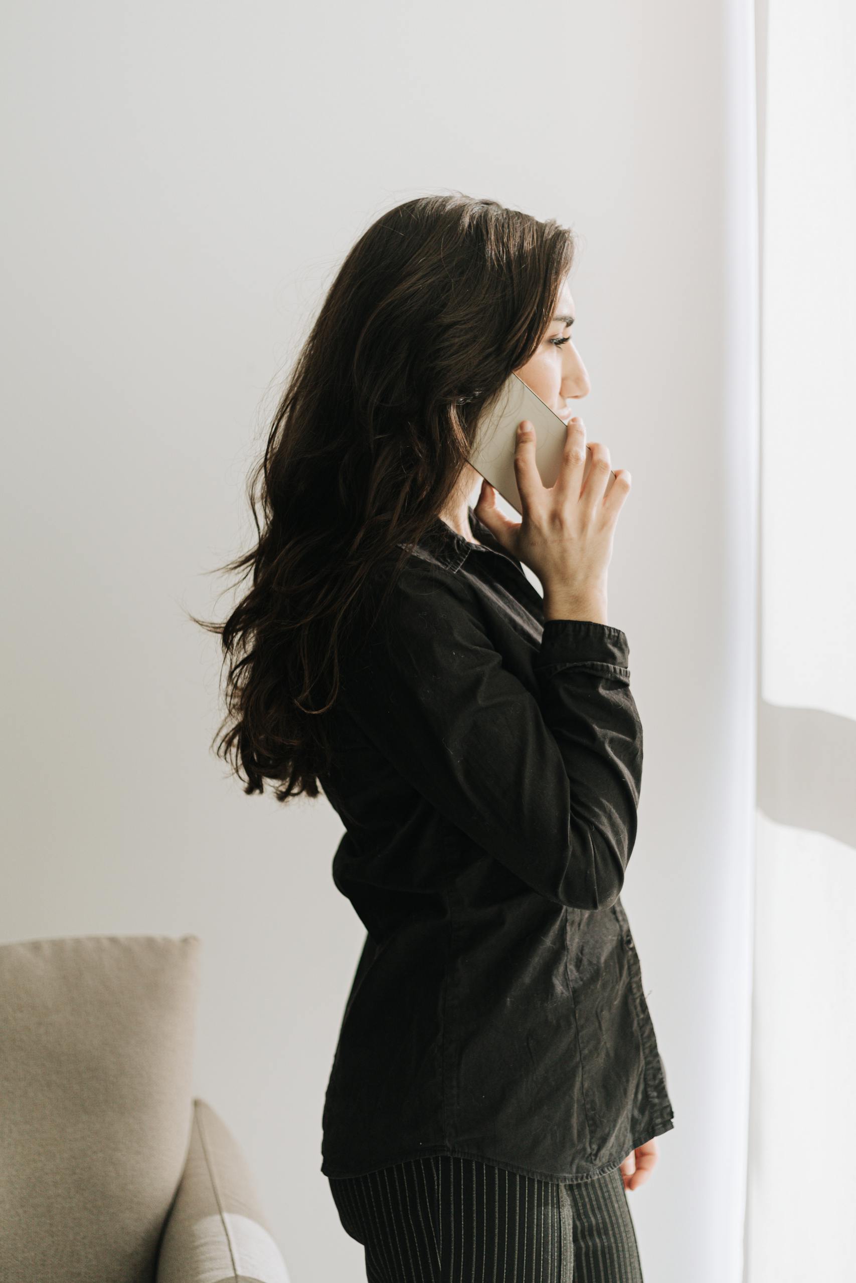 A woman engaged in a phone call in a well-lit office, wearing a black outfit.